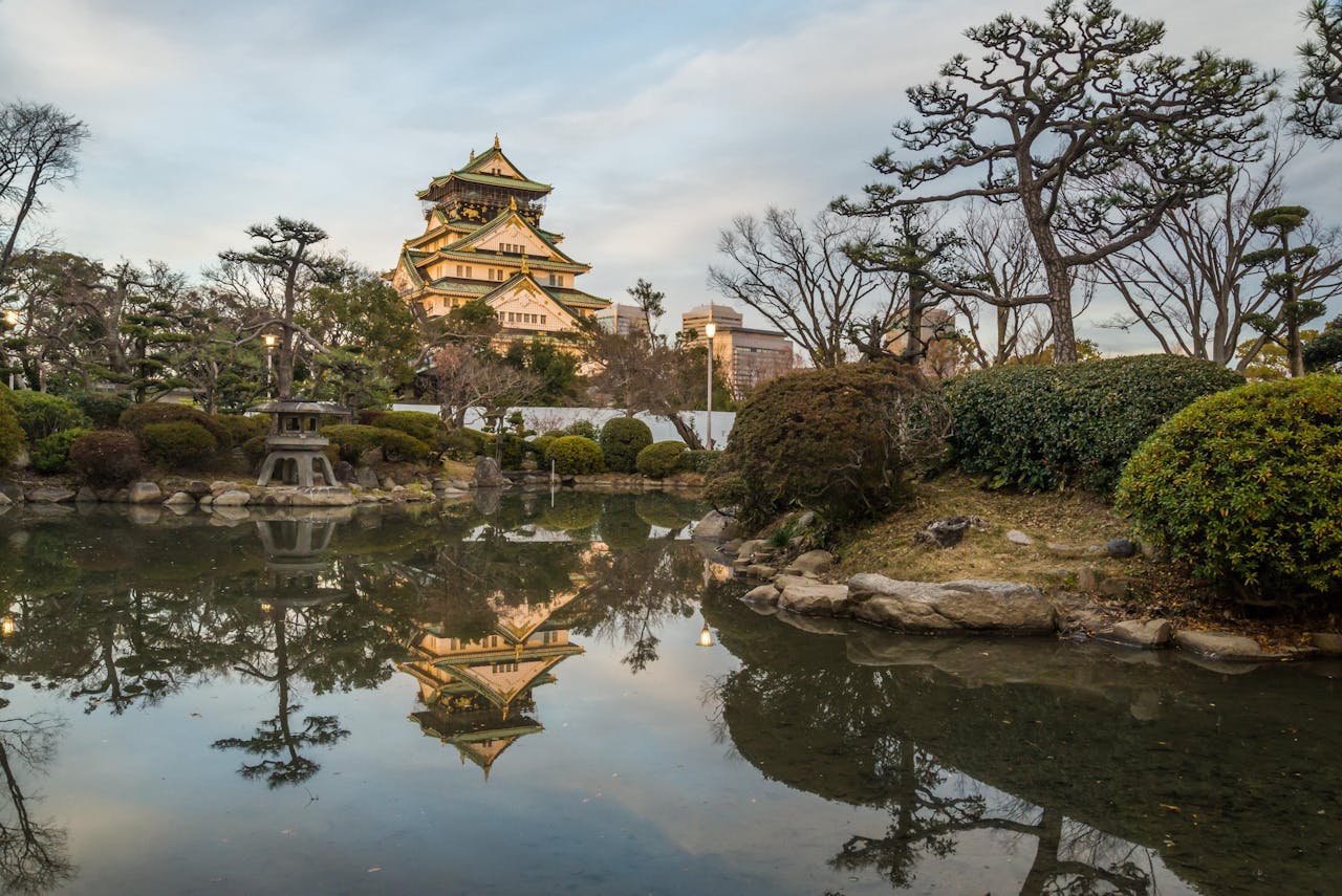Discover the tranquil beauty of Osaka Castle reflecting in a serene garden pond at sunset.