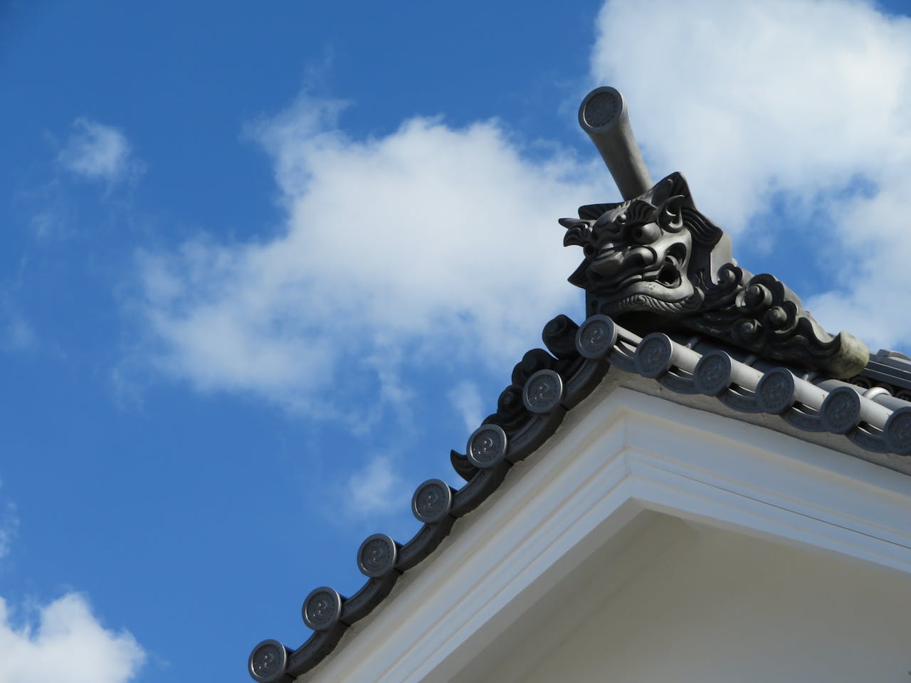 Close-up of a traditional Japanese onigawara rooftop ornament against a vibrant blue sky with clouds.