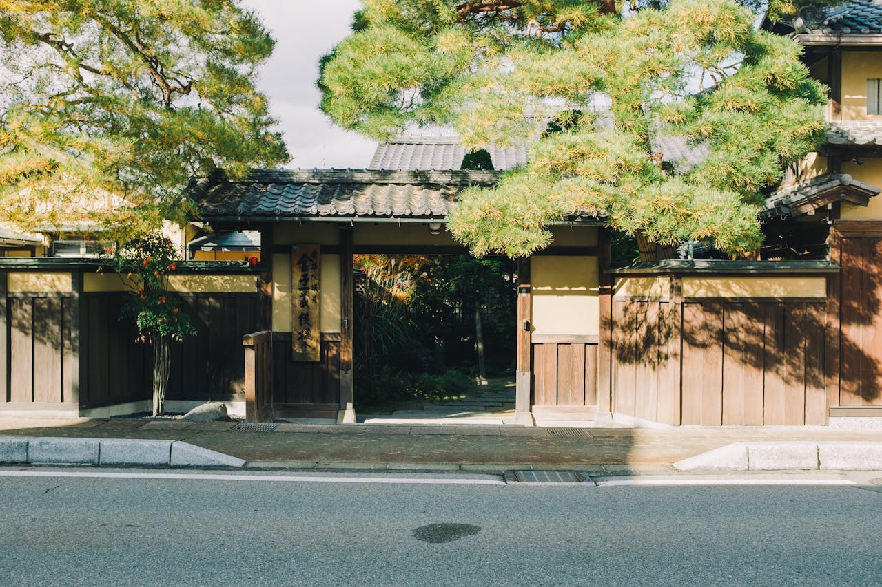 A serene Japanese entrance framed by lush trees, showcasing traditional wooden architecture and cultural elements.